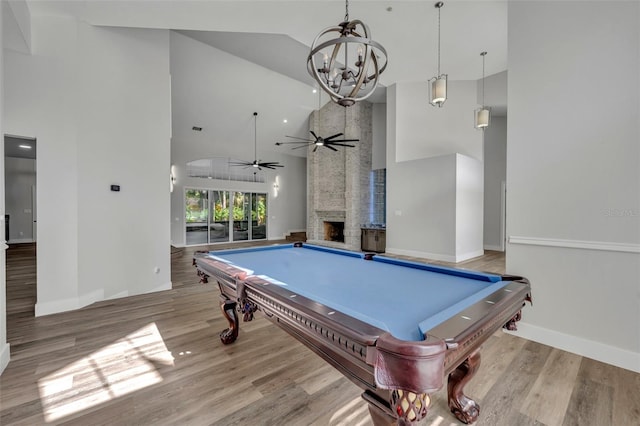 playroom featuring light wood-type flooring, ceiling fan with notable chandelier, high vaulted ceiling, billiards, and a stone fireplace