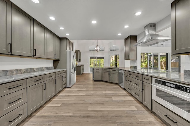 kitchen with light hardwood / wood-style floors, wall chimney range hood, stainless steel appliances, and a wealth of natural light