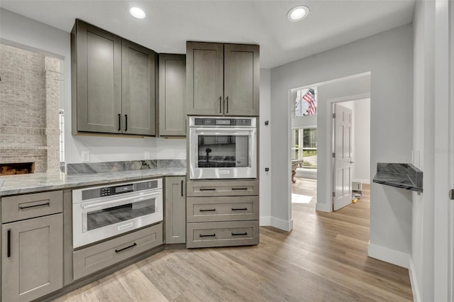 kitchen with light stone countertops, light hardwood / wood-style floors, oven, and gray cabinetry