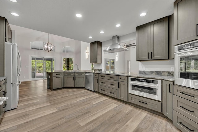 kitchen with gray cabinets, light wood-type flooring, kitchen peninsula, wall chimney exhaust hood, and appliances with stainless steel finishes