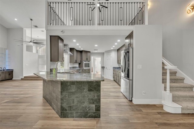 kitchen featuring dark brown cabinetry, kitchen peninsula, sink, wall chimney exhaust hood, and stainless steel fridge with ice dispenser