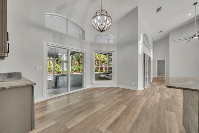 unfurnished dining area featuring ceiling fan with notable chandelier, light hardwood / wood-style flooring, and high vaulted ceiling