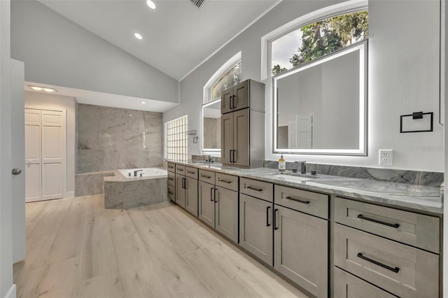 bathroom featuring high vaulted ceiling, wood-type flooring, tiled bath, and vanity