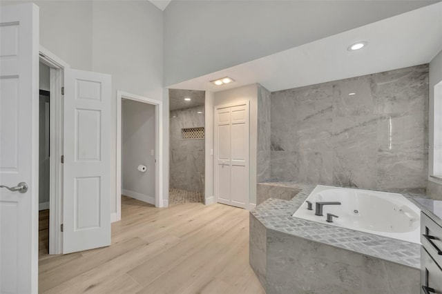 bathroom featuring vanity, separate shower and tub, a towering ceiling, and hardwood / wood-style flooring