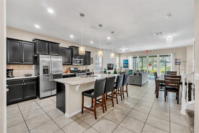 kitchen with a breakfast bar, a kitchen island with sink, hanging light fixtures, decorative backsplash, and appliances with stainless steel finishes