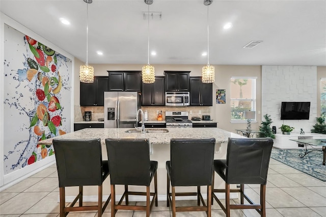 kitchen featuring an island with sink, sink, decorative light fixtures, appliances with stainless steel finishes, and light stone countertops