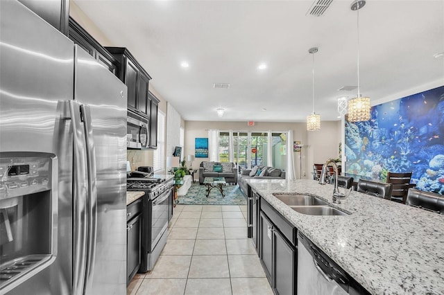 kitchen with light stone counters, light tile patterned floors, stainless steel appliances, decorative light fixtures, and sink