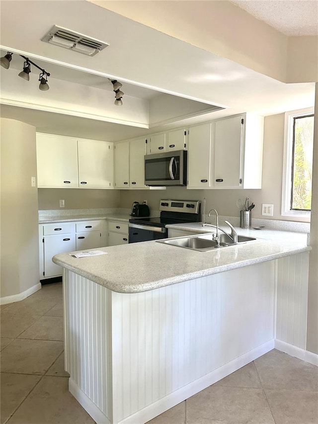 kitchen with sink, light tile patterned floors, appliances with stainless steel finishes, kitchen peninsula, and white cabinets