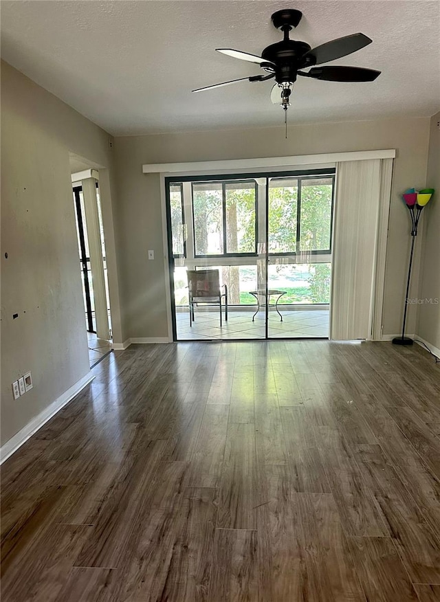 empty room with a wealth of natural light, ceiling fan, dark wood-type flooring, and a textured ceiling