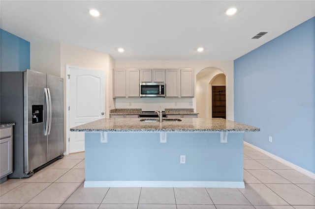 kitchen with light stone countertops, an island with sink, appliances with stainless steel finishes, and sink