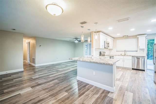 kitchen featuring stainless steel appliances, hanging light fixtures, kitchen peninsula, and white cabinetry