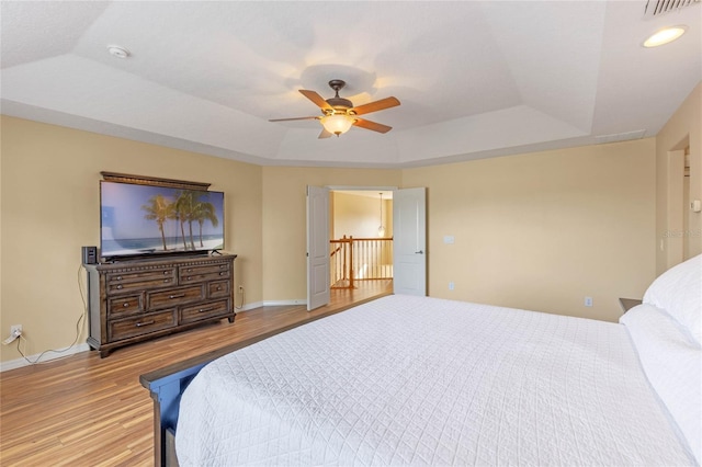 bedroom featuring ceiling fan, a tray ceiling, and light hardwood / wood-style flooring