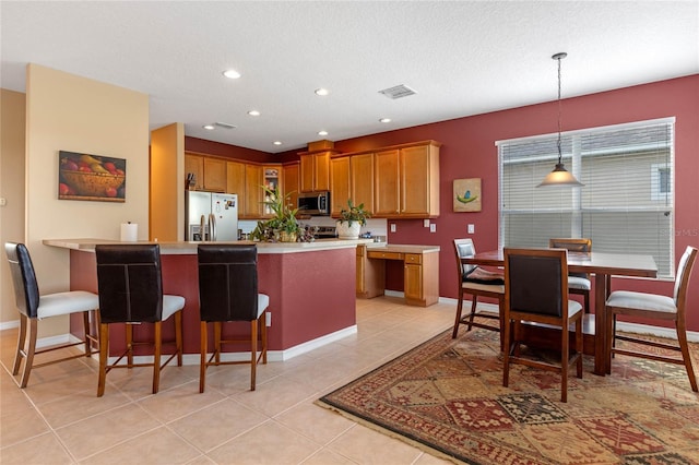 kitchen with a textured ceiling, light tile patterned floors, hanging light fixtures, and appliances with stainless steel finishes