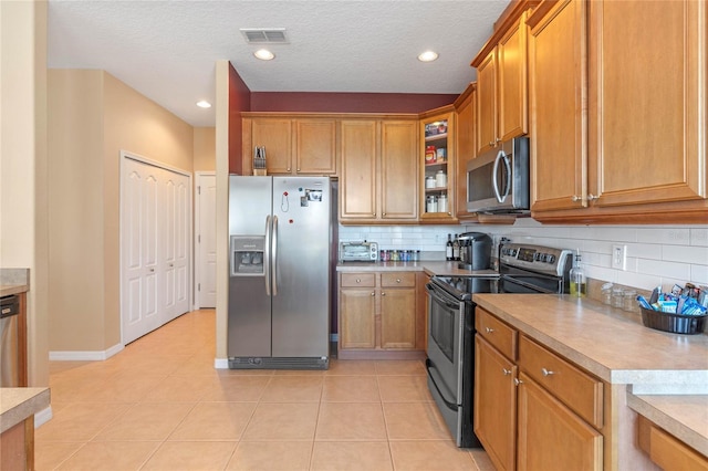 kitchen featuring appliances with stainless steel finishes, a textured ceiling, tasteful backsplash, and light tile patterned floors