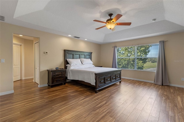 bedroom with ceiling fan, dark hardwood / wood-style flooring, a raised ceiling, and a textured ceiling