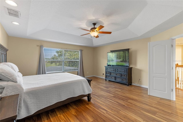 bedroom featuring ceiling fan, light wood-type flooring, a textured ceiling, and a tray ceiling