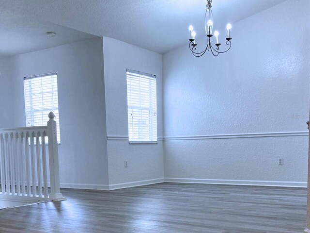 empty room with a notable chandelier, a wealth of natural light, and dark hardwood / wood-style flooring