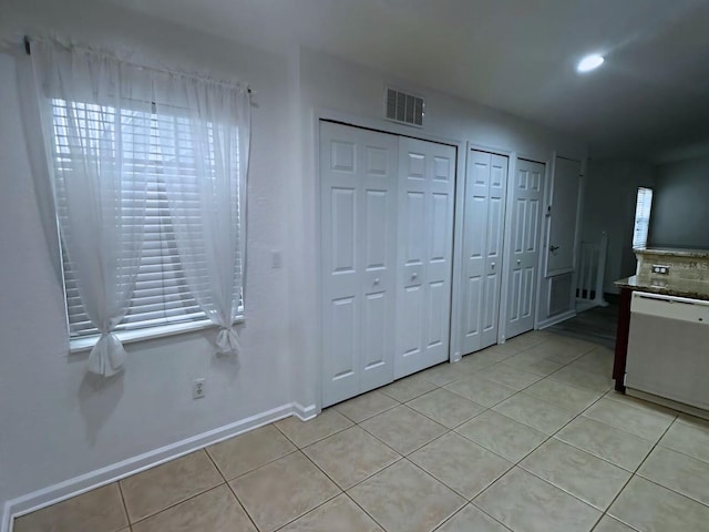 unfurnished bedroom with multiple windows, light tile patterned floors, and multiple closets