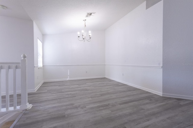 spare room with hardwood / wood-style flooring, an inviting chandelier, and a textured ceiling