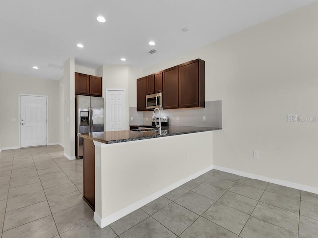 kitchen featuring dark stone countertops, light tile patterned flooring, stainless steel appliances, and kitchen peninsula