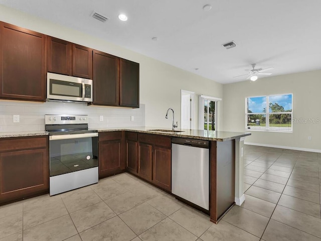 kitchen featuring light stone counters, sink, kitchen peninsula, appliances with stainless steel finishes, and ceiling fan