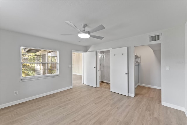 unfurnished bedroom featuring ceiling fan, ensuite bathroom, a closet, a spacious closet, and light hardwood / wood-style floors