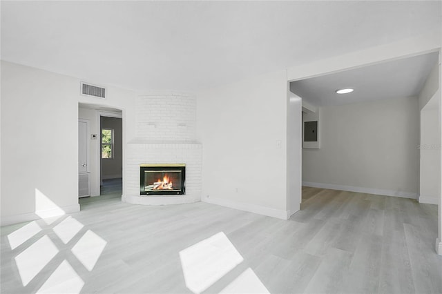 unfurnished living room with a brick fireplace, light wood-type flooring, and electric panel