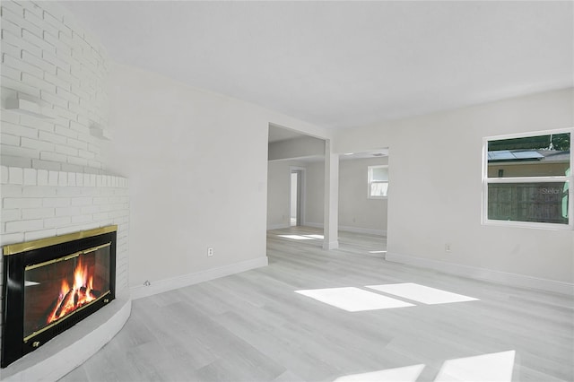 unfurnished living room with a brick fireplace and light hardwood / wood-style flooring