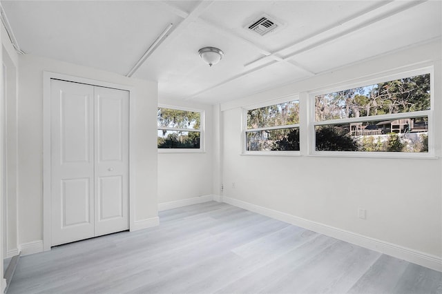 unfurnished bedroom with light hardwood / wood-style flooring, coffered ceiling, a closet, and multiple windows