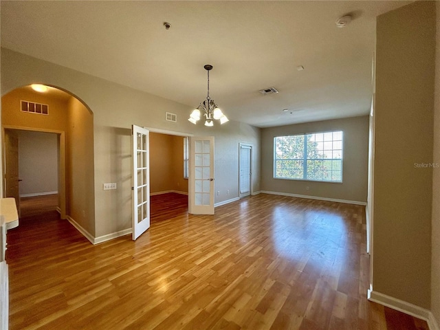 spare room featuring a notable chandelier, hardwood / wood-style floors, and french doors