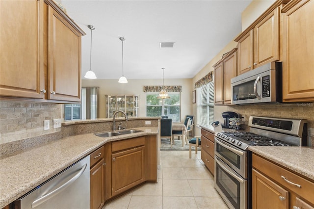 kitchen with light stone countertops, stainless steel appliances, hanging light fixtures, and sink