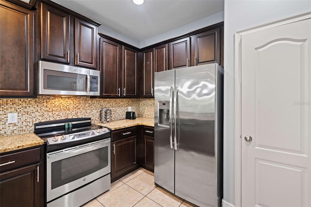 kitchen featuring tasteful backsplash, appliances with stainless steel finishes, light tile patterned flooring, dark brown cabinetry, and light stone counters