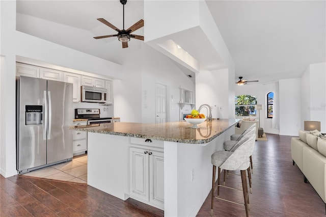 kitchen with appliances with stainless steel finishes, hardwood / wood-style flooring, vaulted ceiling, and an island with sink