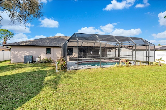 rear view of house with a lawn, glass enclosure, and a fenced in pool