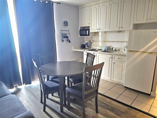 kitchen with sink, white cabinetry, light hardwood / wood-style flooring, decorative backsplash, and white appliances