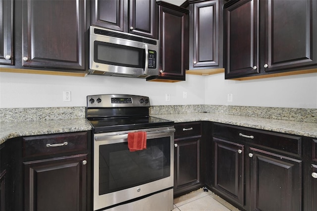 kitchen featuring dark brown cabinets, light stone countertops, stainless steel appliances, and light tile patterned floors