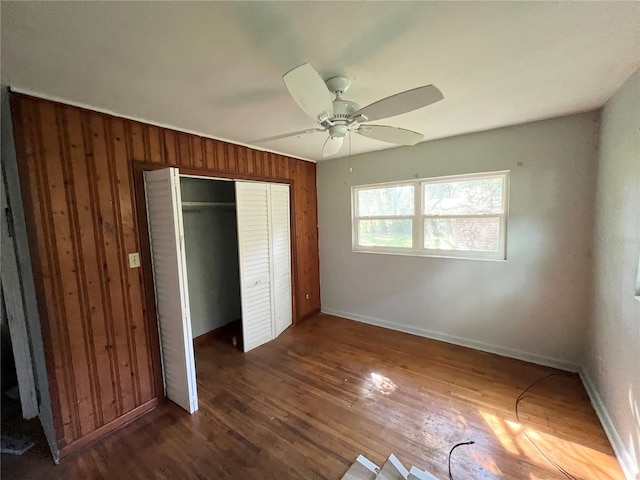 unfurnished bedroom featuring wood walls, dark hardwood / wood-style floors, ceiling fan, and a closet