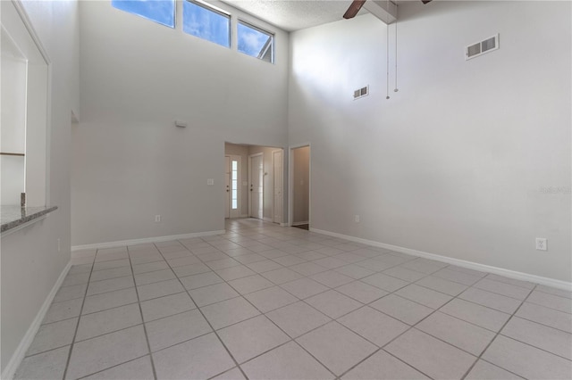 tiled empty room with ceiling fan, high vaulted ceiling, and a textured ceiling