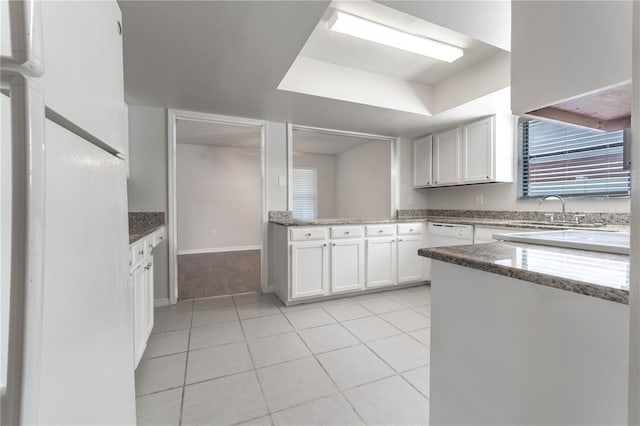 kitchen with kitchen peninsula, dark stone countertops, sink, light tile patterned floors, and white cabinetry