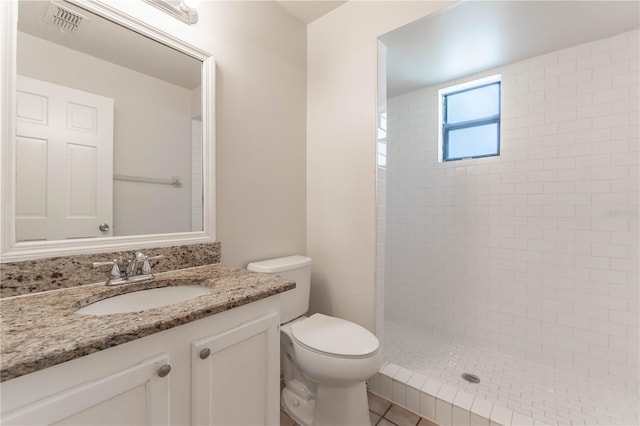 bathroom featuring vanity, toilet, a tile shower, and tile patterned flooring