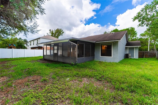 rear view of property featuring a sunroom, a lawn, and central AC unit