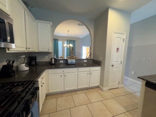 kitchen with white cabinets, appliances with stainless steel finishes, arched walkways, an inviting chandelier, and light tile patterned flooring