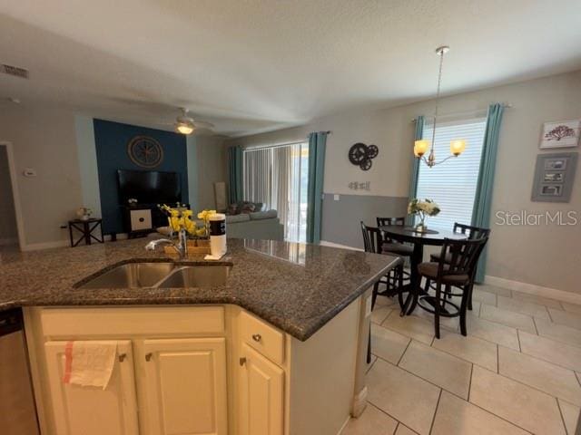 kitchen with pendant lighting, dark stone counters, sink, light tile patterned floors, and stainless steel dishwasher