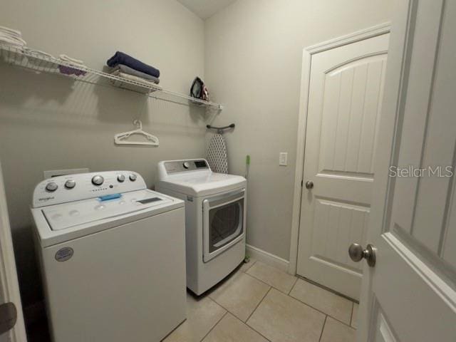 washroom featuring light tile patterned flooring, separate washer and dryer, laundry area, and baseboards
