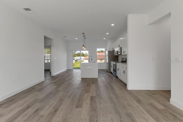 kitchen with appliances with stainless steel finishes, hanging light fixtures, white cabinets, light hardwood / wood-style flooring, and a center island with sink