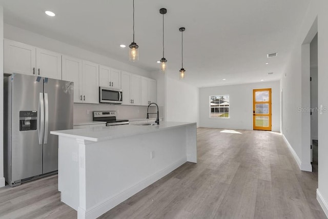 kitchen featuring appliances with stainless steel finishes, white cabinetry, a kitchen island with sink, light hardwood / wood-style flooring, and decorative light fixtures