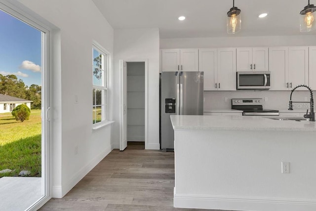 kitchen featuring sink, hanging light fixtures, white cabinetry, stainless steel appliances, and light hardwood / wood-style flooring