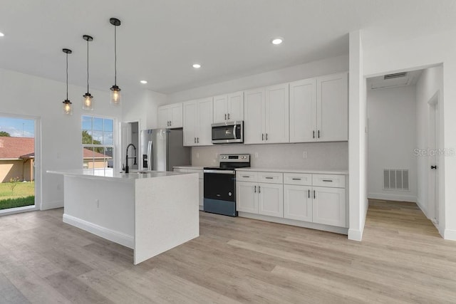 kitchen featuring appliances with stainless steel finishes, light wood-type flooring, white cabinetry, pendant lighting, and a kitchen island with sink