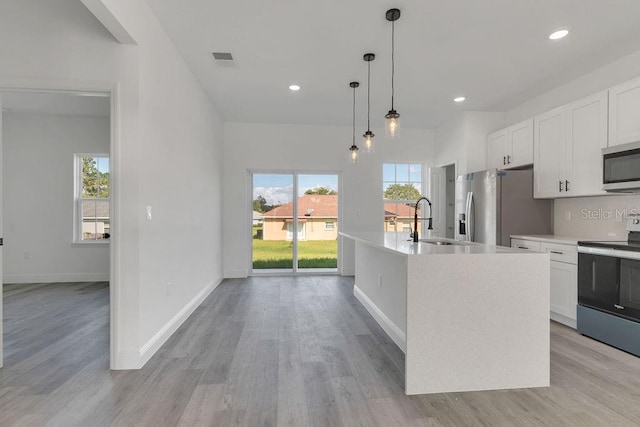 kitchen featuring light hardwood / wood-style floors, stainless steel appliances, decorative light fixtures, white cabinets, and a kitchen island with sink