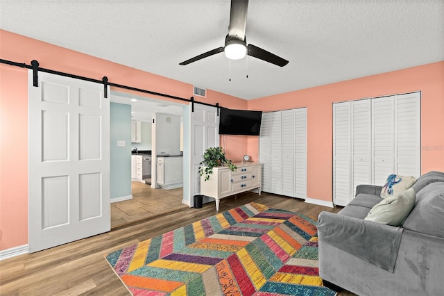 bedroom with ceiling fan, hardwood / wood-style flooring, a barn door, a textured ceiling, and two closets